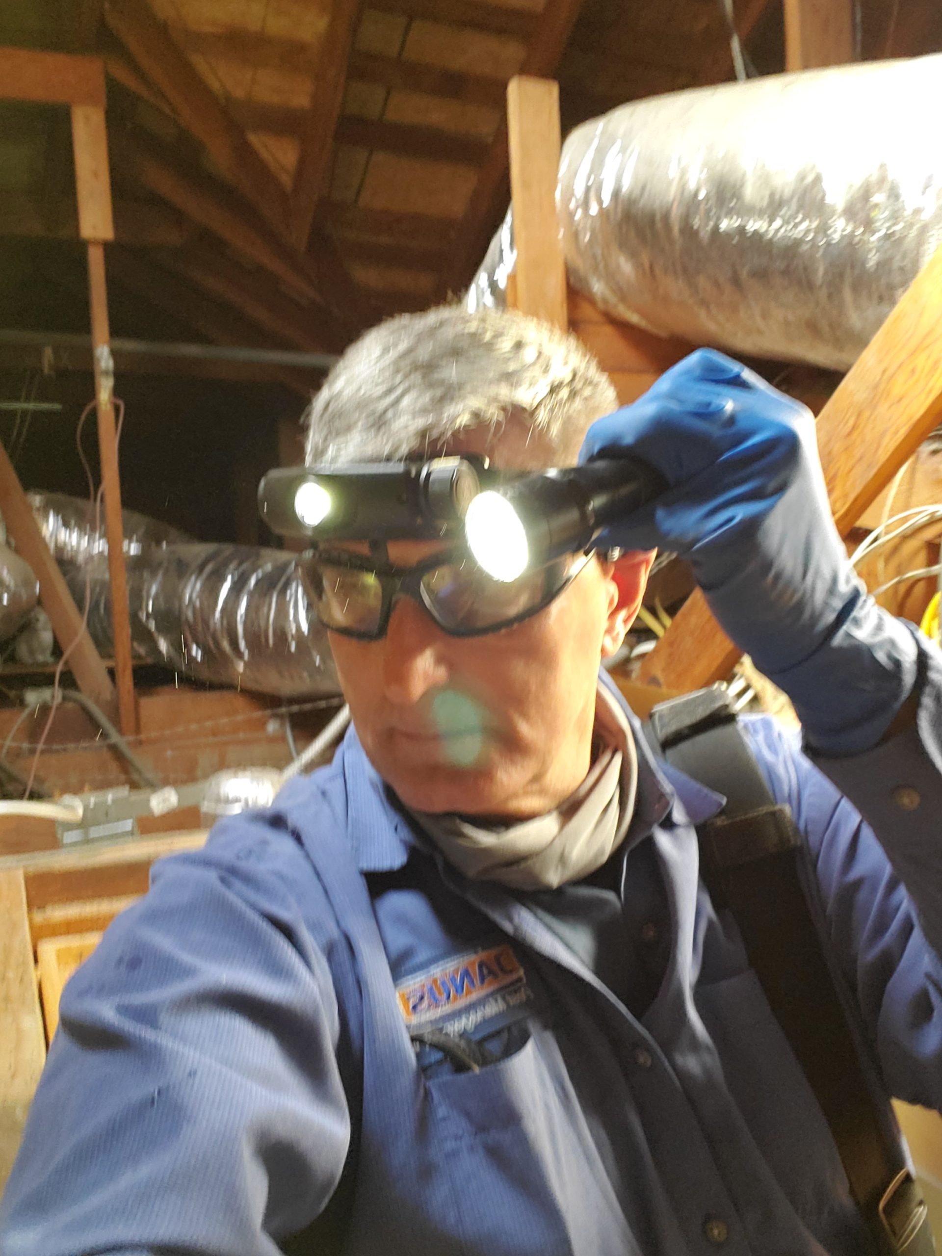 Janus Pest Management technician conducting rodent inspection in residential attic — headlamp and protective gear, Los Angeles